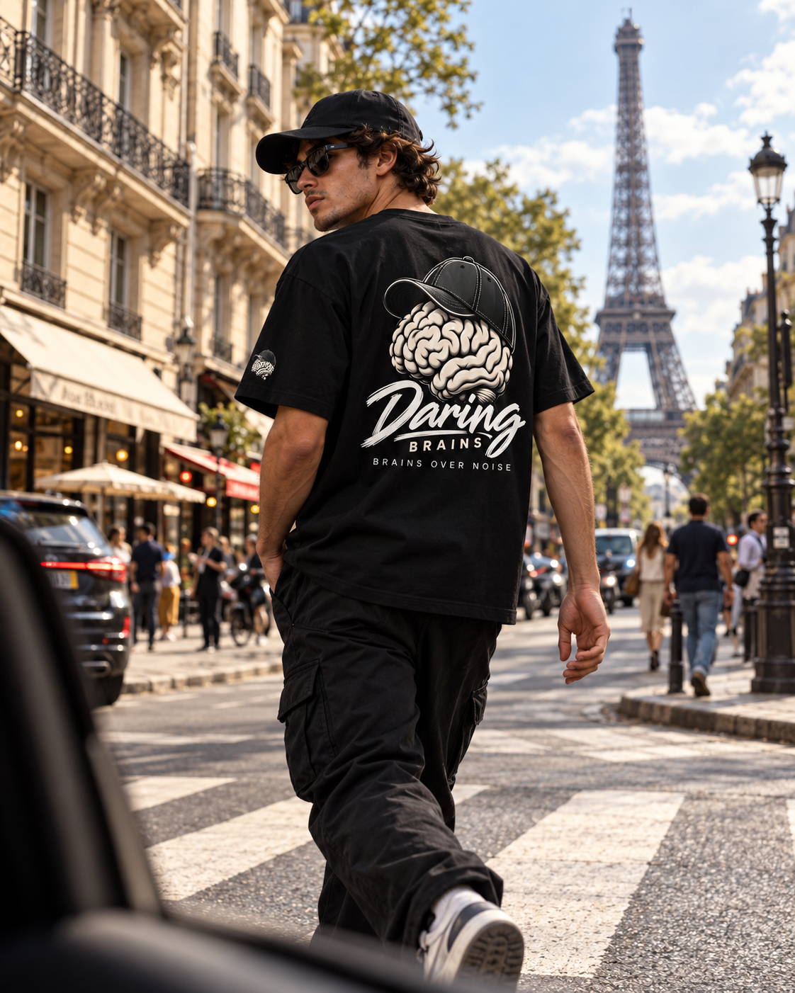 Chico de espaldas con camiseta negra Daring Brains, logo grande en la espalda, cruzando una calle